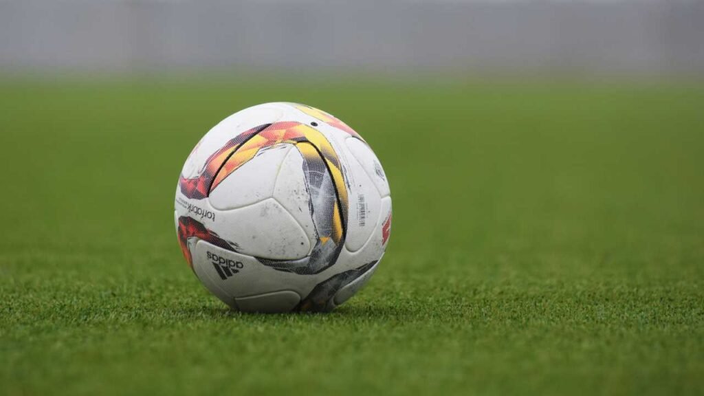Vemos una pelota de color blanco con líneas de varios colores en la cancha